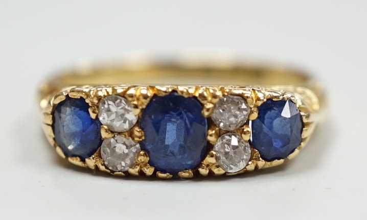 A late Victorian 18ct gold and three stone sapphire set ring, with four stone diamond set spacers, size M, gross weight 4.1 grams.